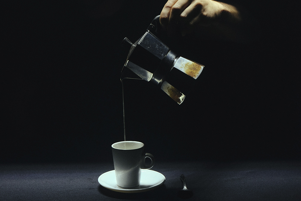 Mà que aboca cafè d'una cafetera cap a una tassa blanca sobre un plat blanc.