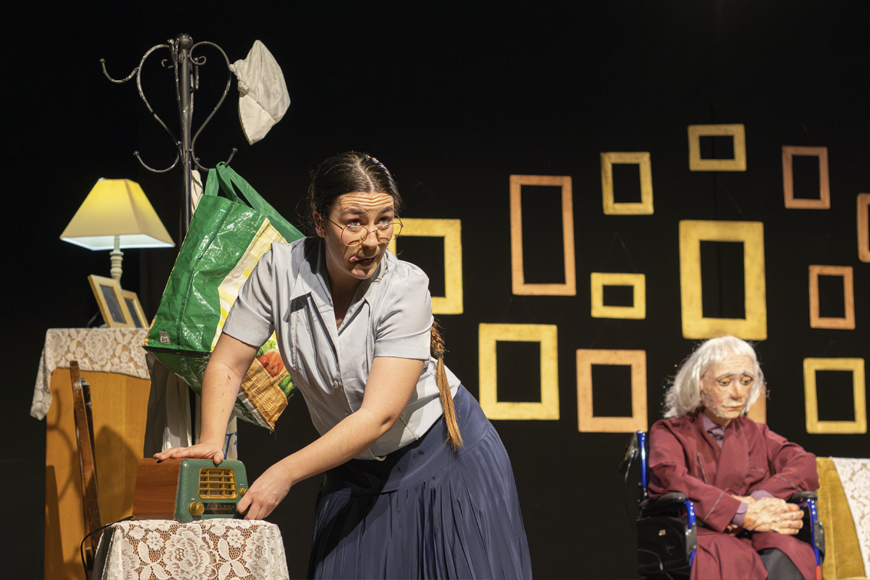 "A woman in a dark stage with old radio, taking care of her father."